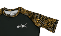 Close-up of GuardX logo on Batik-X Inferno rashguard chest, black fabric with yellow and brown batik details